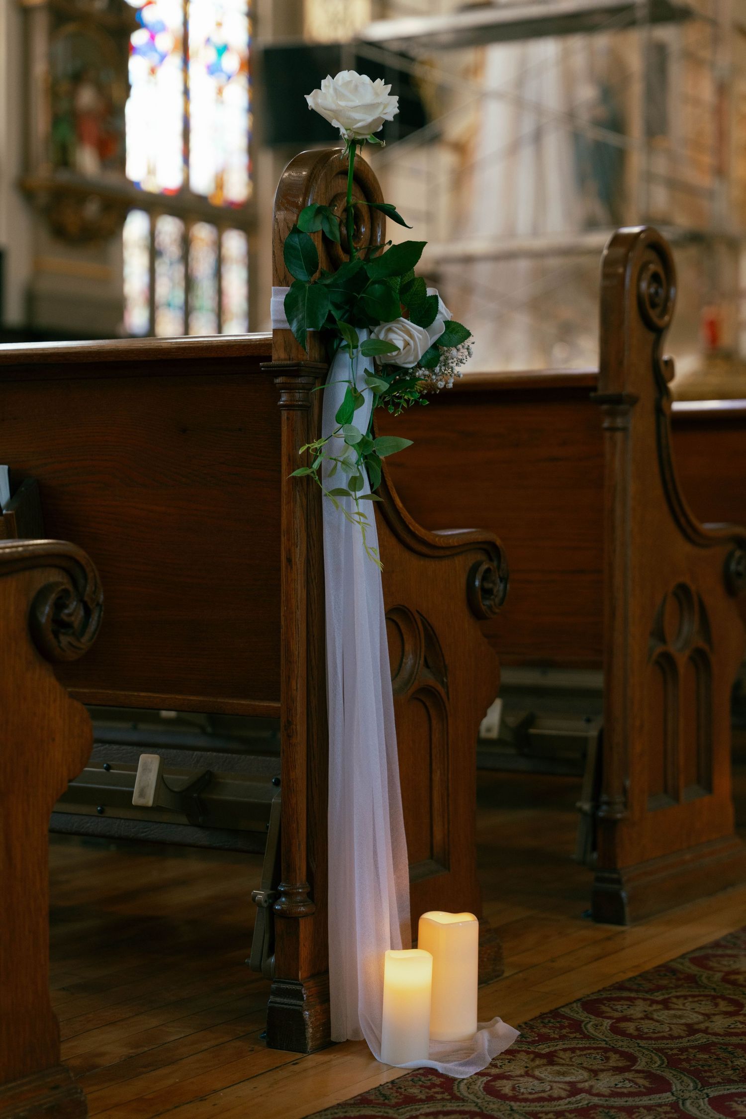 White rose and candles decorating wooden church pew aisle for wedding ceremony.