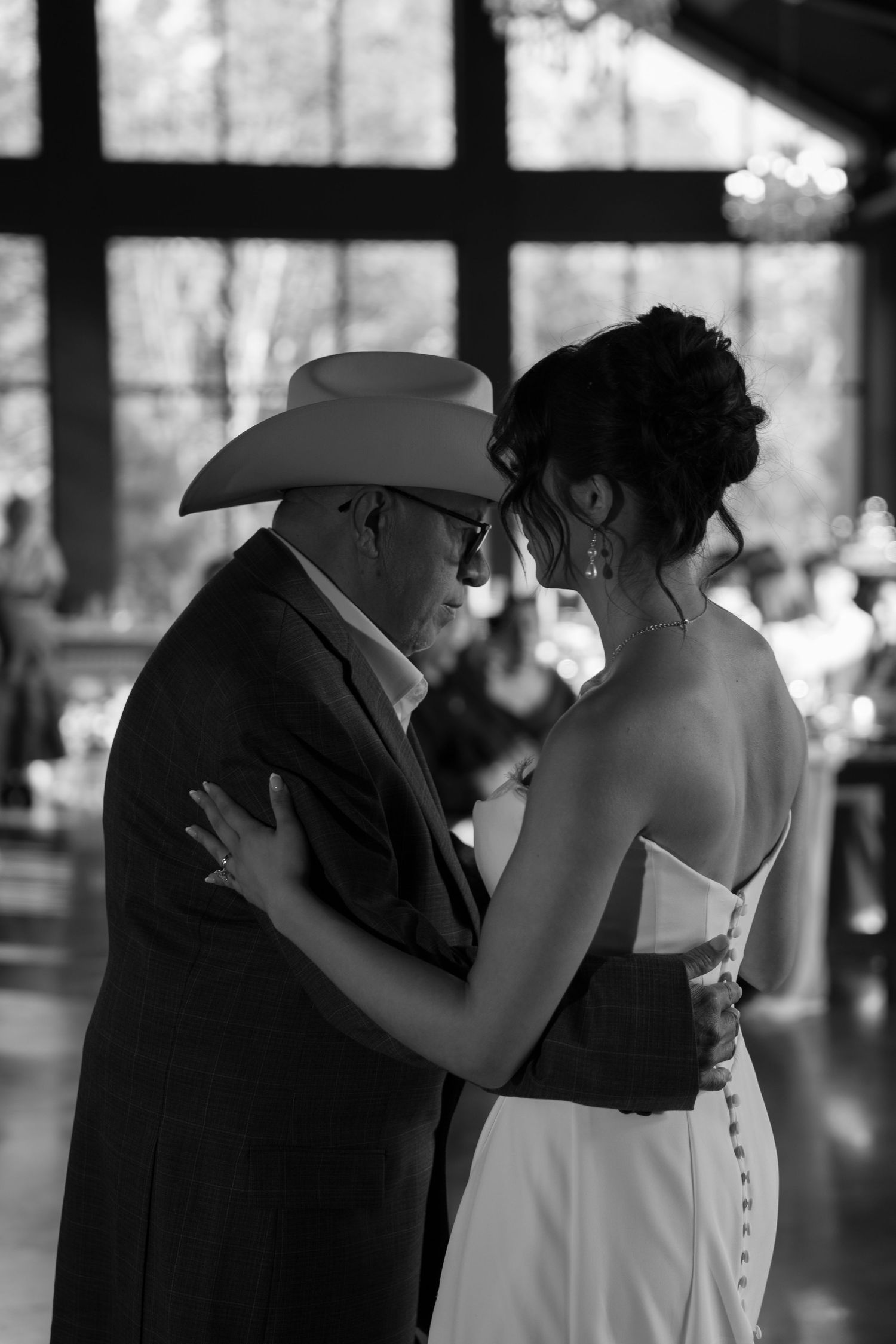 Bride shares emotional father-daughter dance with man in cowboy hat at elegant black and white wedding reception.