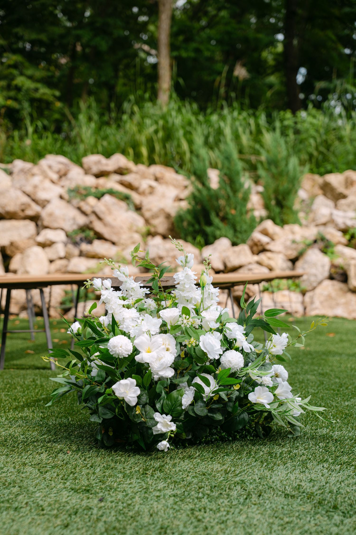 Elegant white floral arrangement with roses and greenery on green lawn at outdoor wedding ceremony.