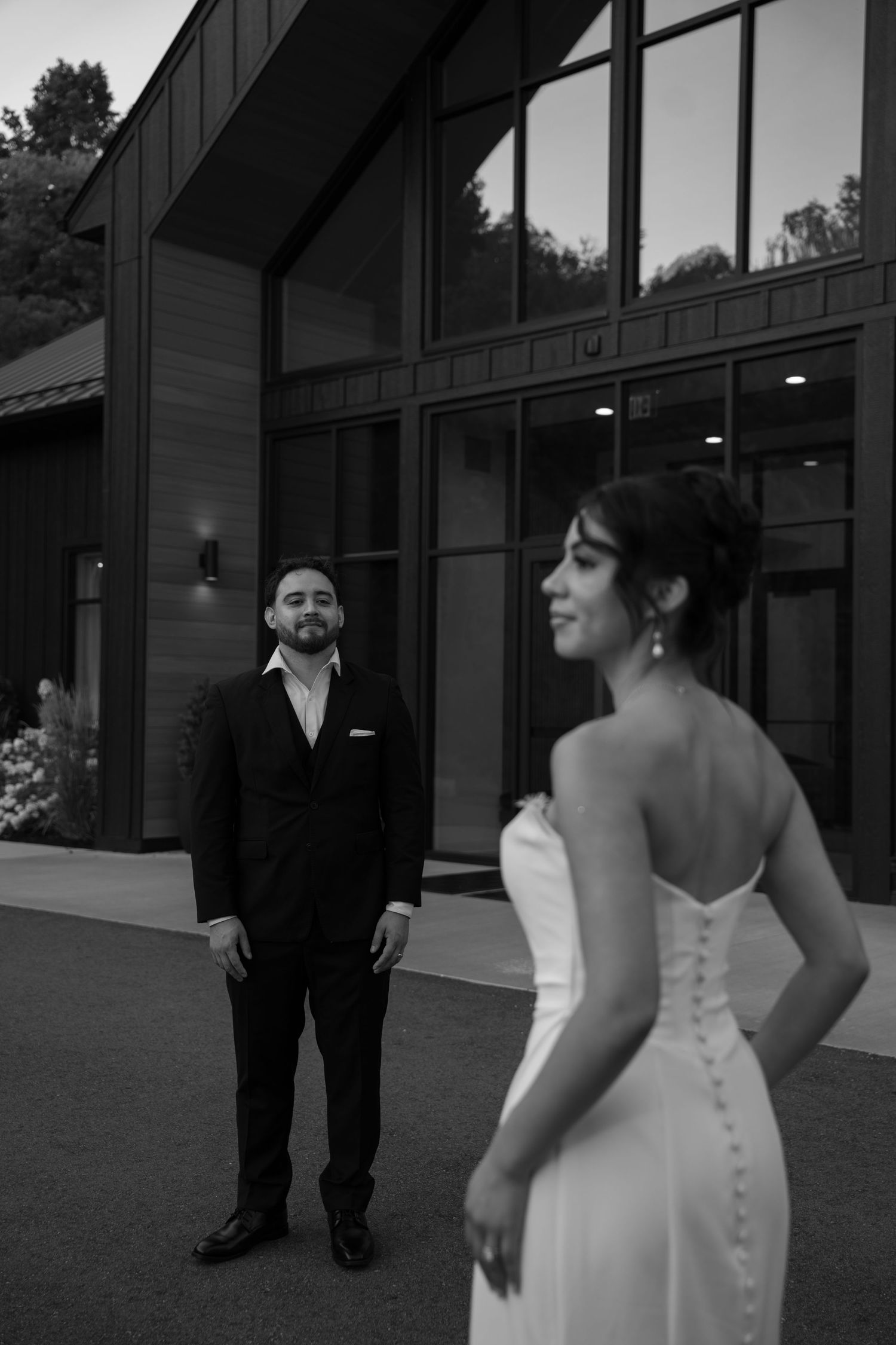 Groom gazes at bride in a black and white portrait outside an elegant modern venue.
