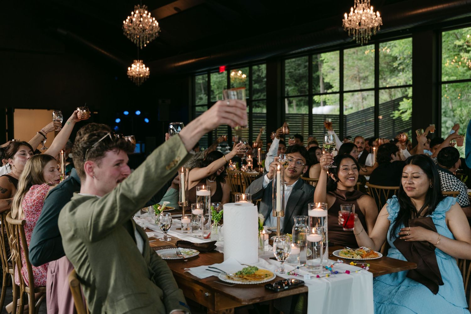 Wedding guests raise glasses in a toast at a candlelit reception in an elegant venue.