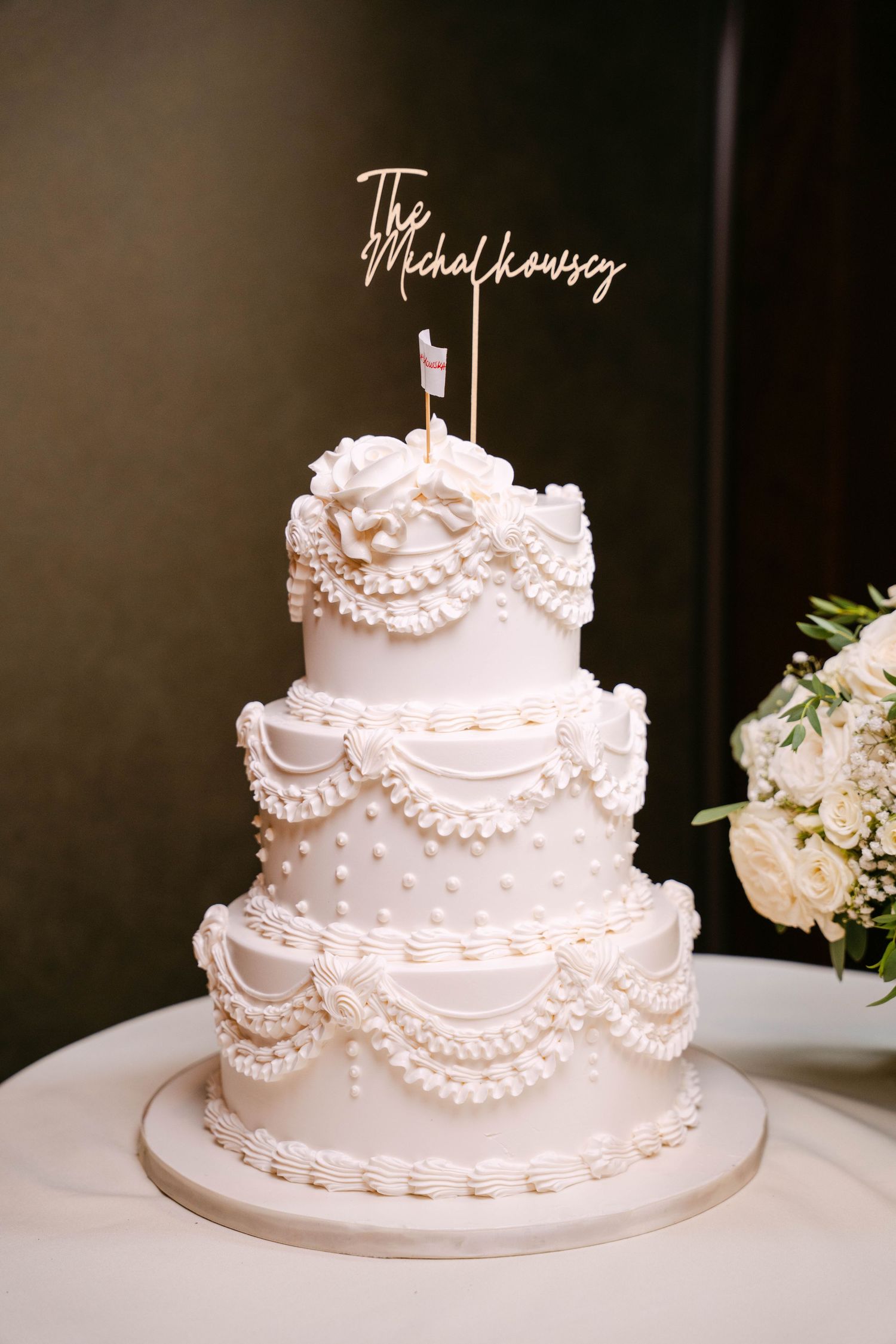 Three-tier white wedding cake with pearl details and The Michalkowsey cake topper.