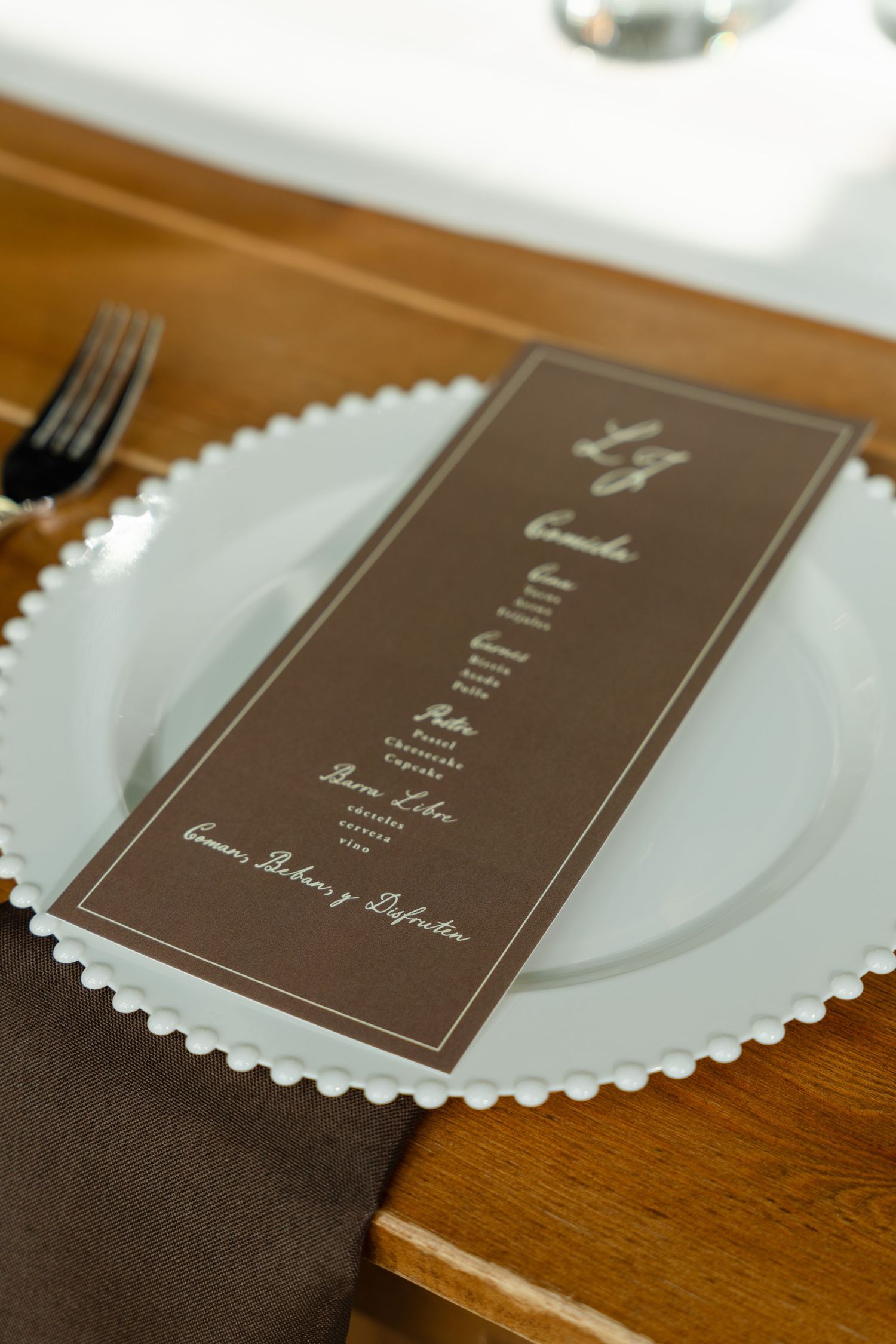 Brown wedding menu card on beaded charger plate with fork and folded napkin.