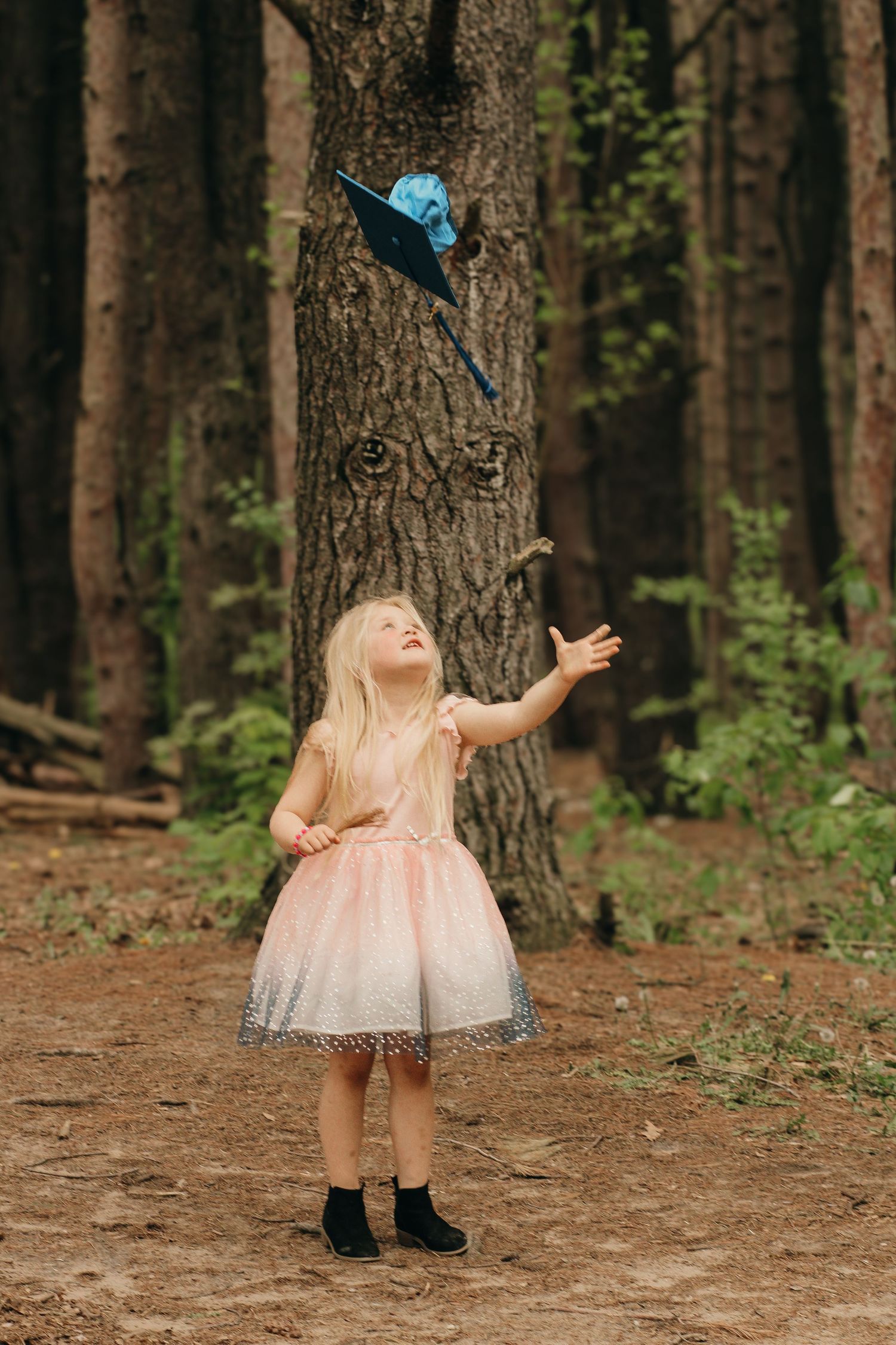 A young blonde girl in a pink tutu dress tosses a blue umbrella in a forest.