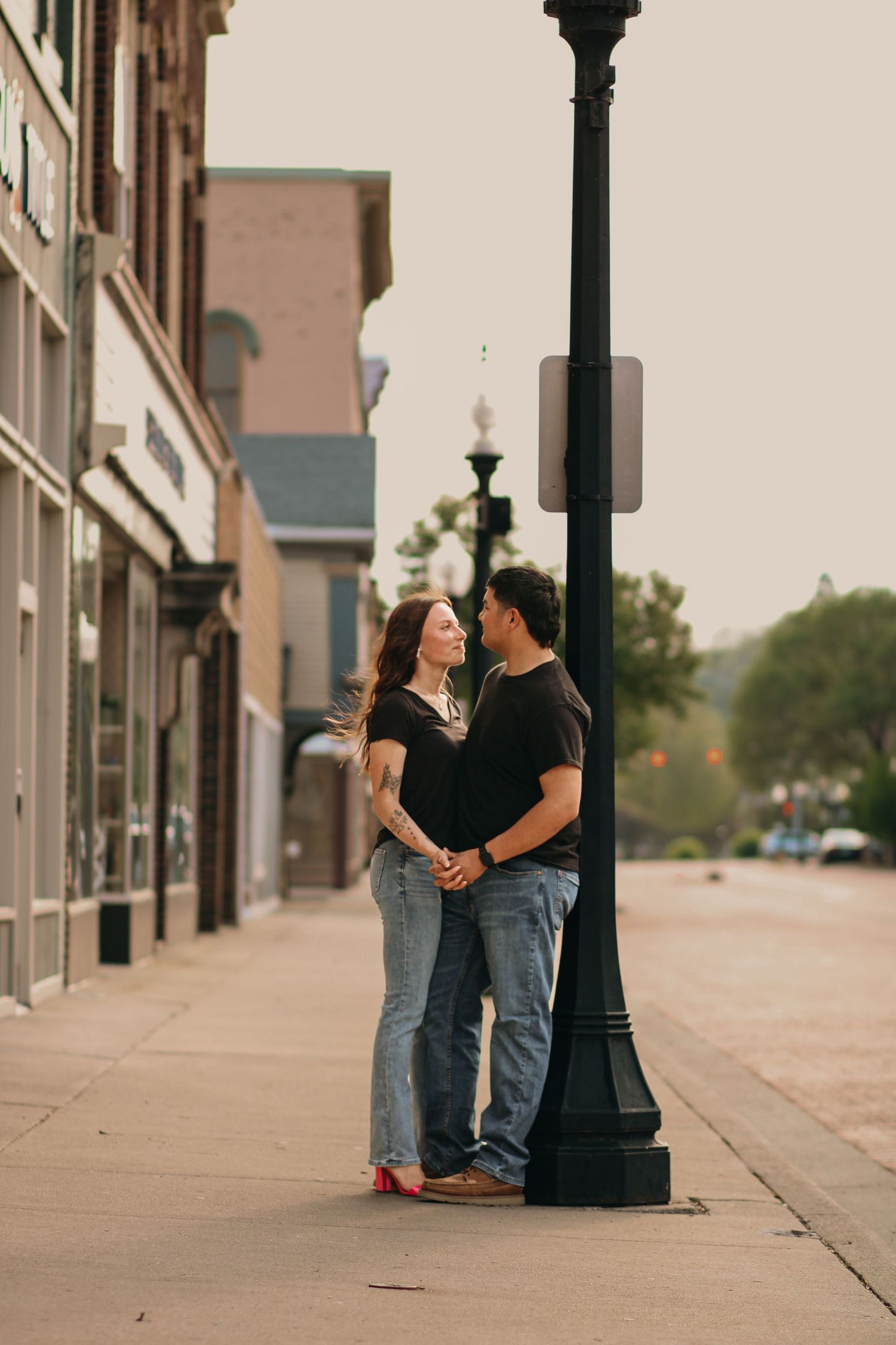 Romantic couple nearly kissing beside a street lamp on a quiet small-town sidewalk.