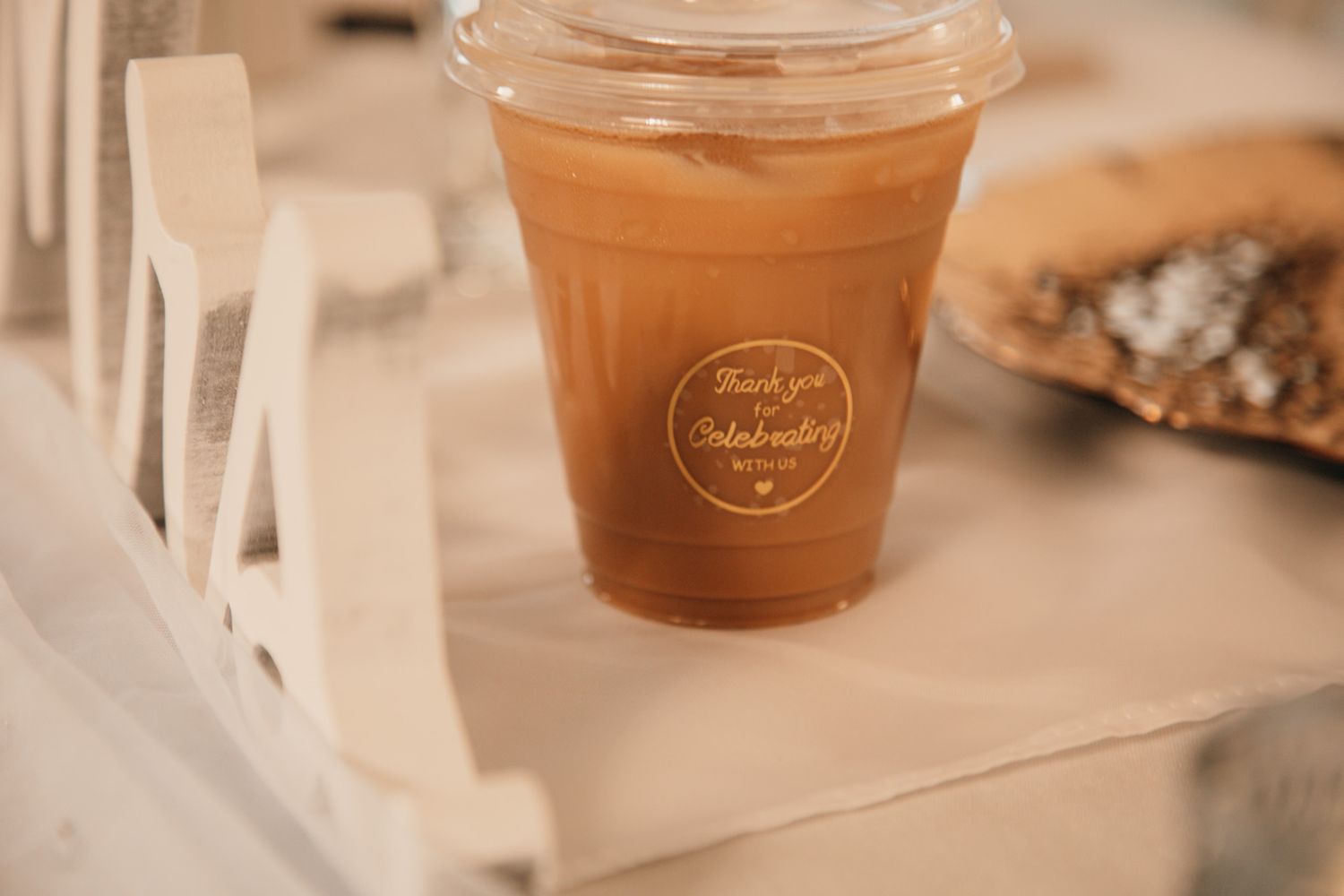 Iced coffee drink in a clear plastic cup with a branded sticker, placed on a white wooden tray.