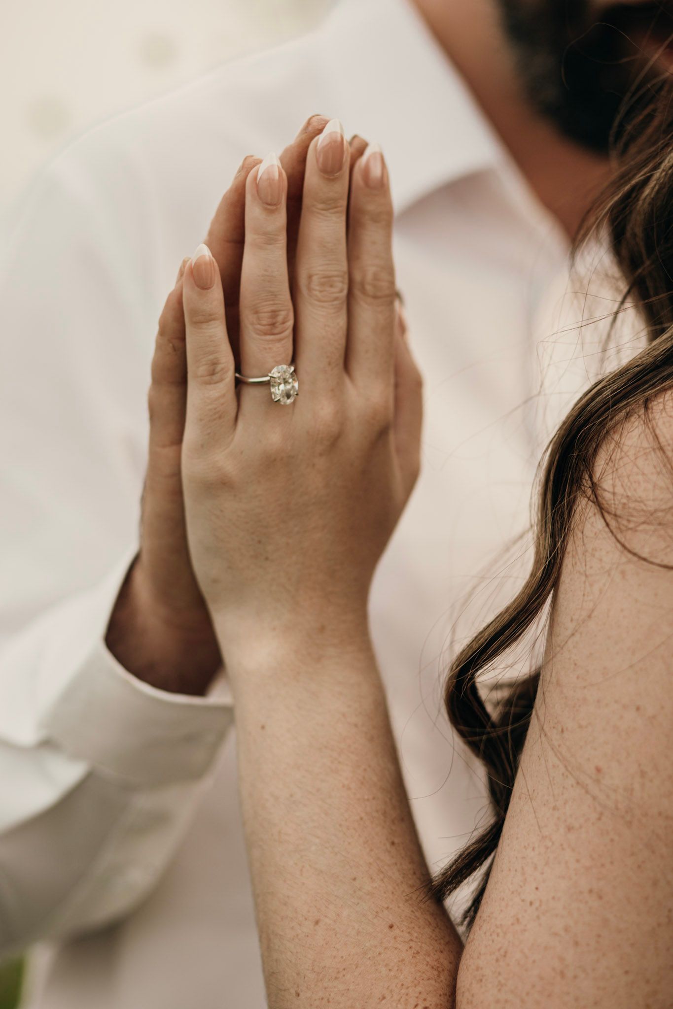 Close-up of a woman's hand displaying a diamond engagement ring pressed against a man's white shirt.