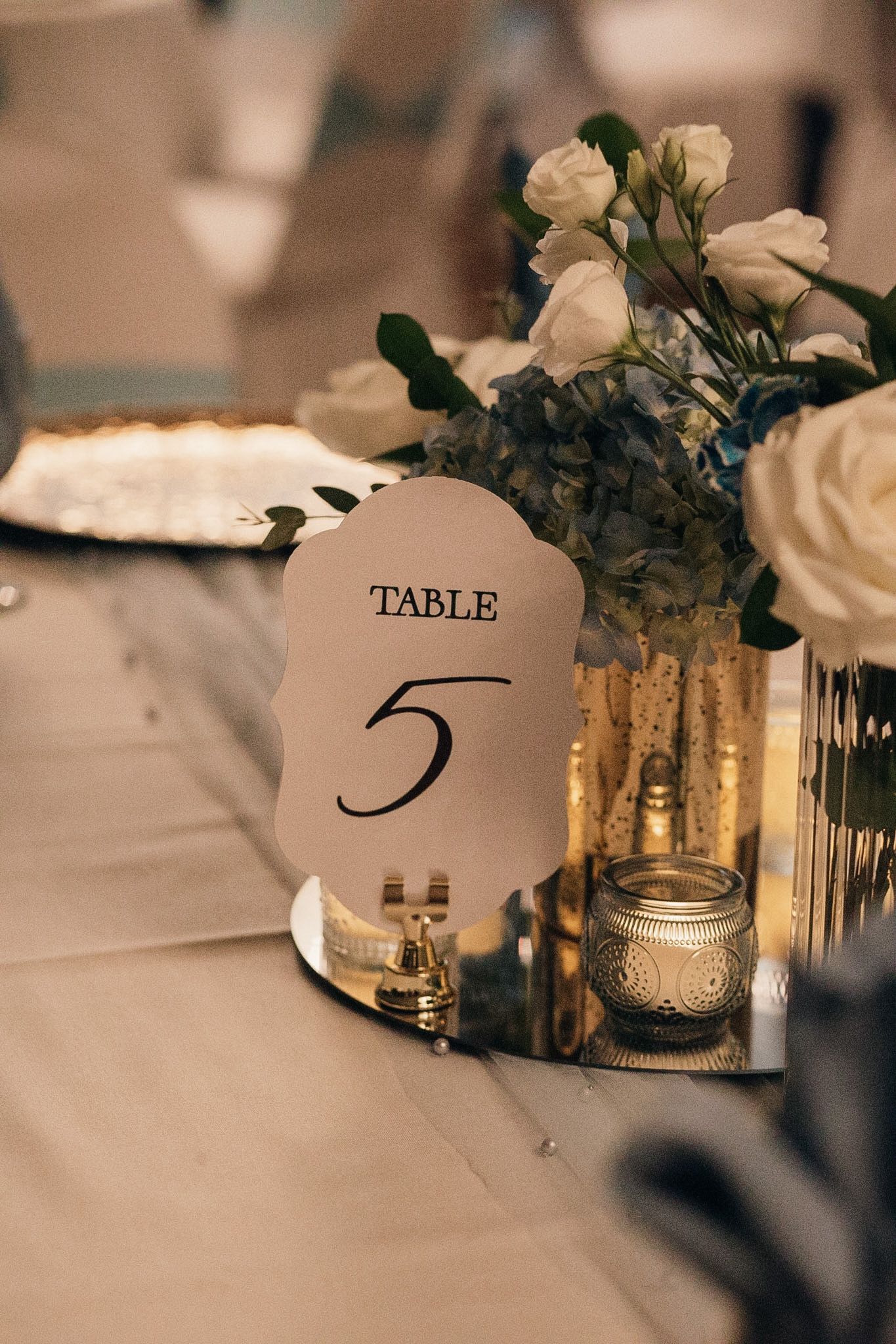 Elegant wedding table 5 setting with white and blue floral centerpiece, gold candle holders, and mirrored tray.
