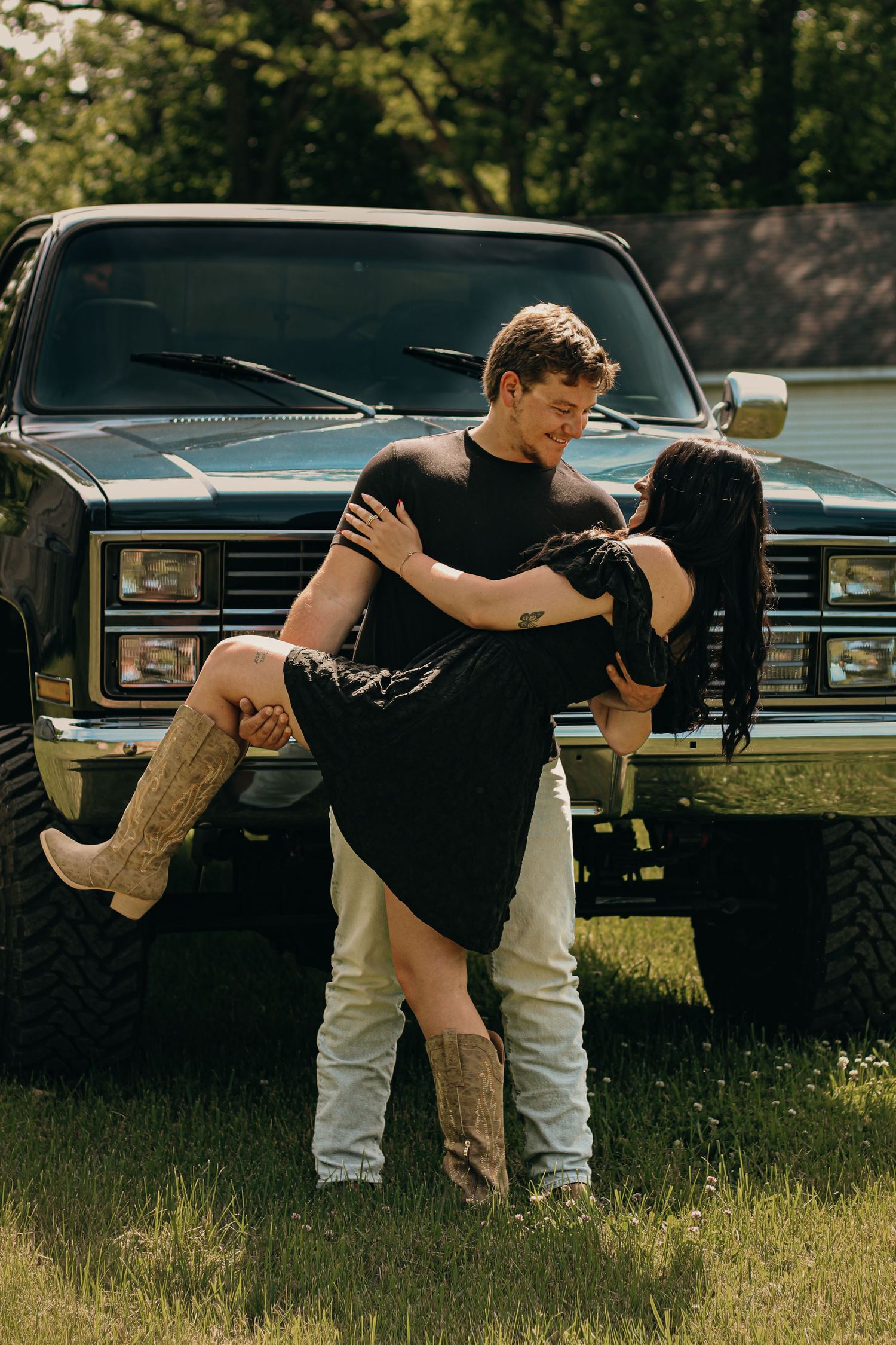 Couple posing romantically in front of a vintage black pickup truck outdoors.