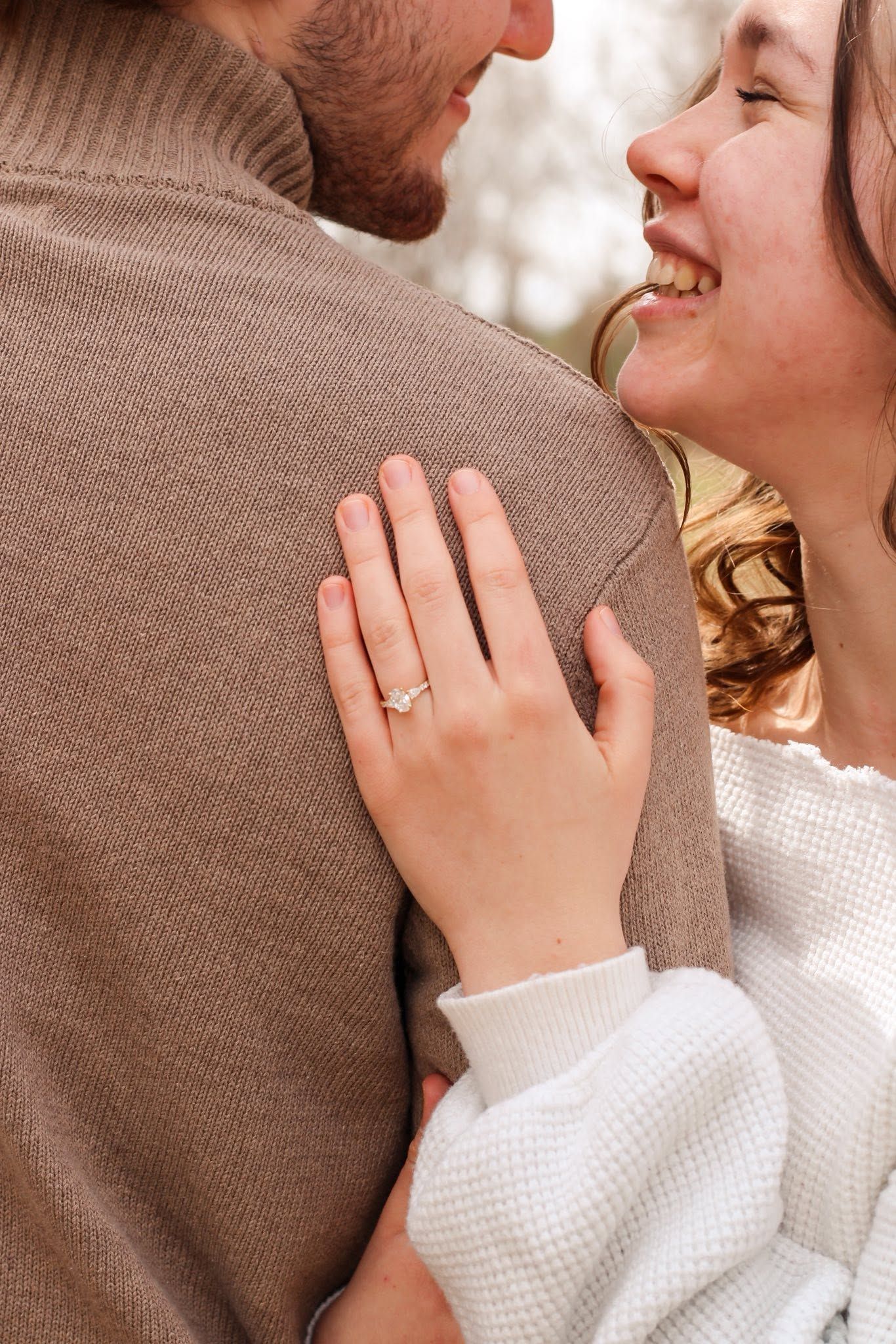 Close-up of smiling woman showing diamond engagement ring on hand while embracing her partner.