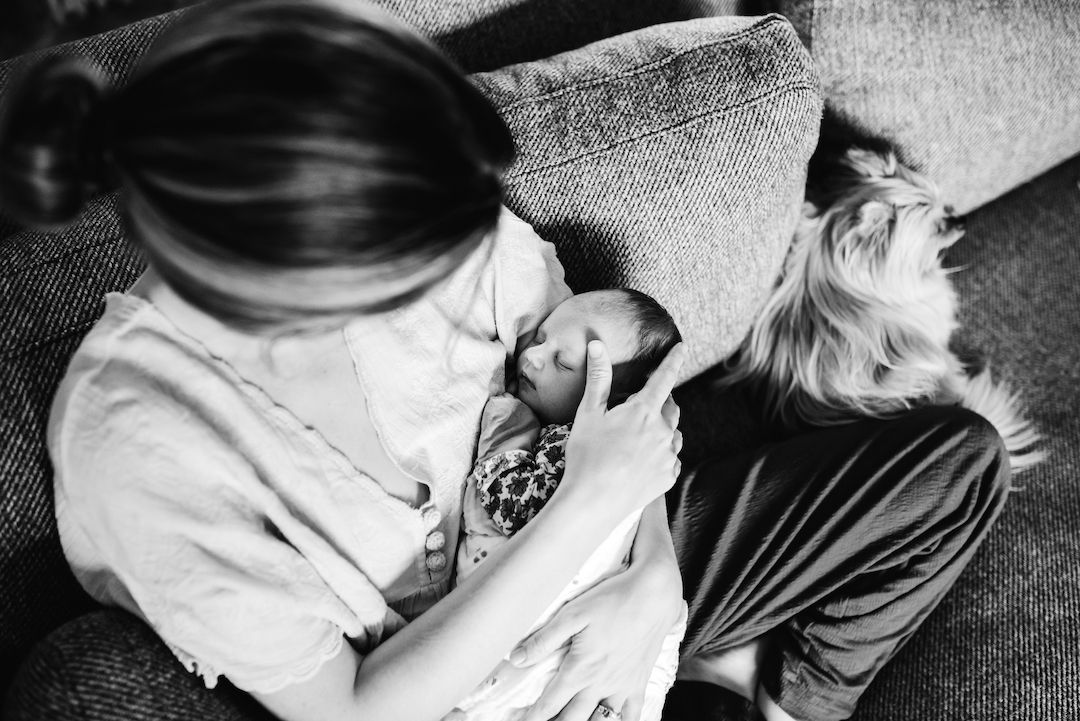 Black and white photo of a mother breastfeeding her newborn baby while an older child looks on.