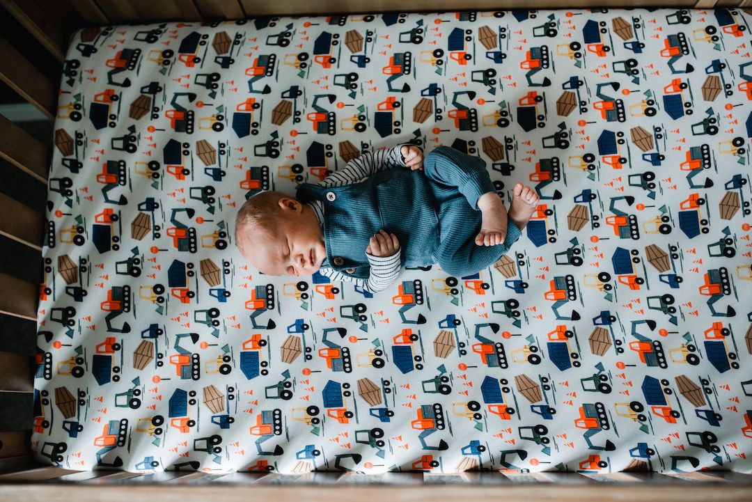 Baby sleeping peacefully in a crib on a colorful construction vehicle patterned fitted sheet.
