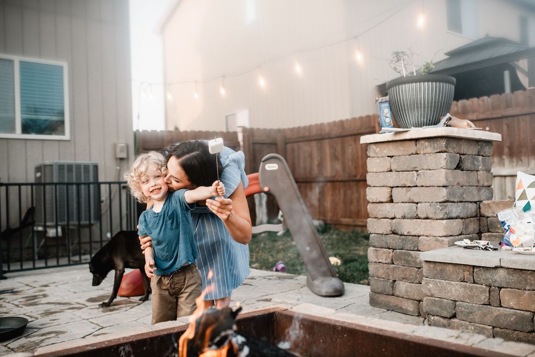 Mother kissing her young son on the cheek in a backyard patio at sunset.