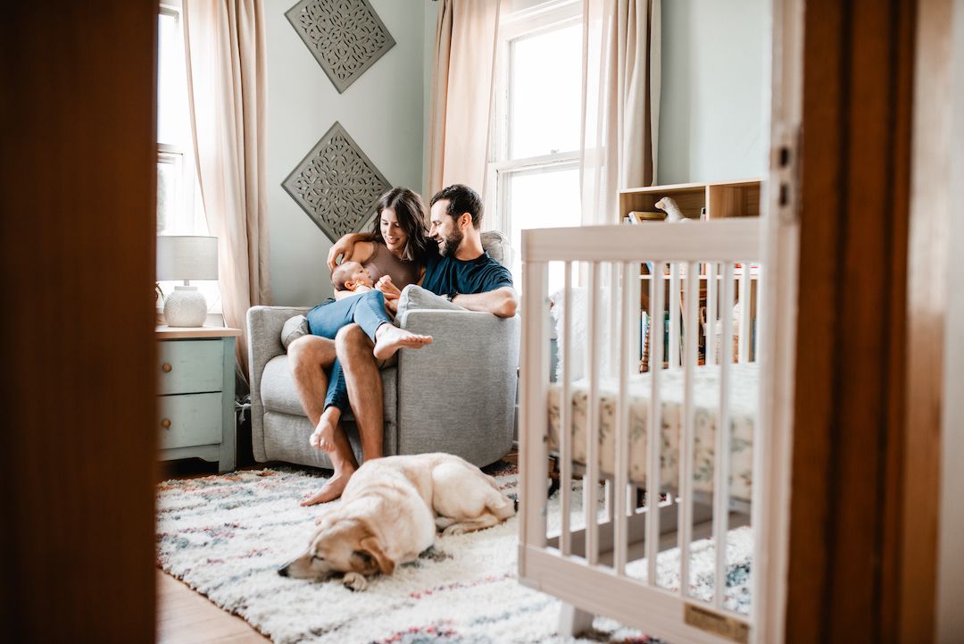 Young family reading together in a nursery with a golden retriever resting nearby.