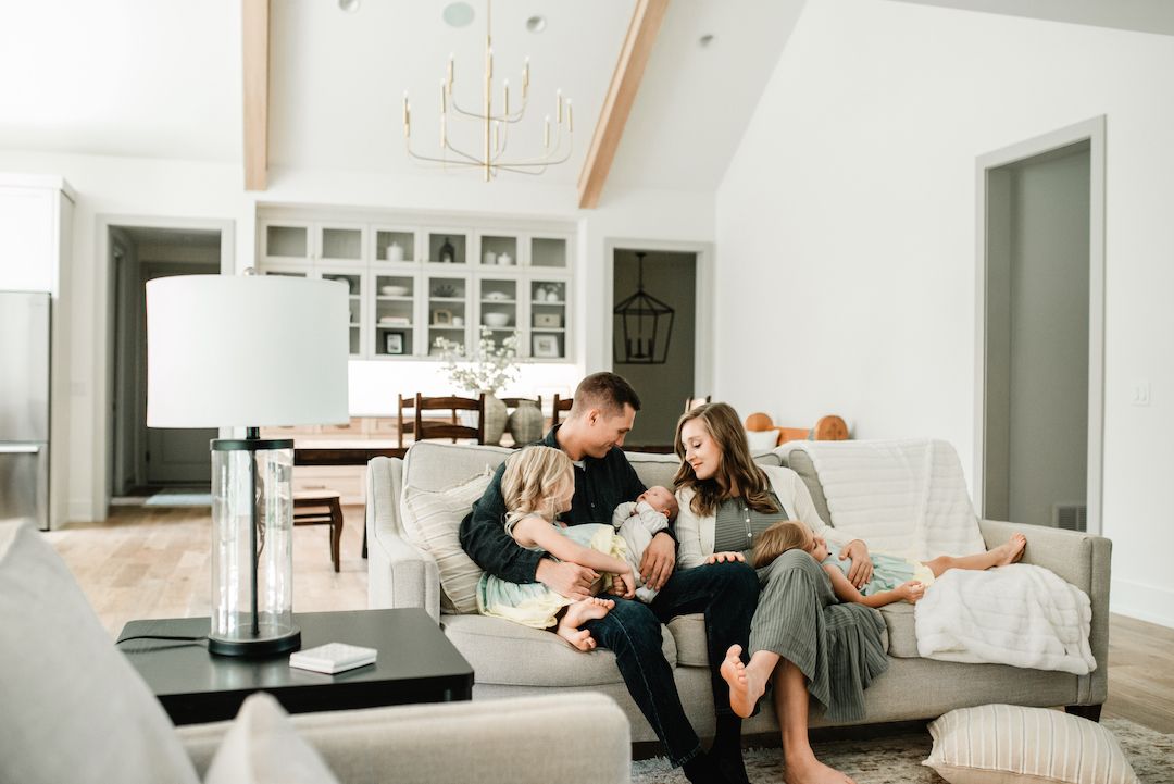 Family sitting together on a couch in a bright living room, parents bonding with their newborn baby.