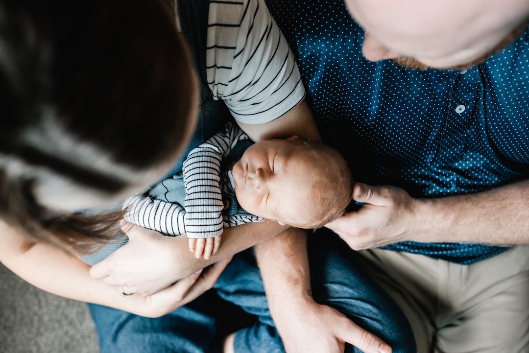 Parents cradling their newborn baby, viewed from above, with gentle hands supporting the infant.