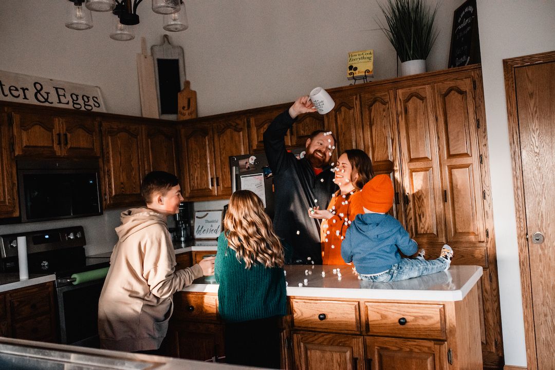 Family laughing and having fun together in a rustic kitchen with wooden cabinets.