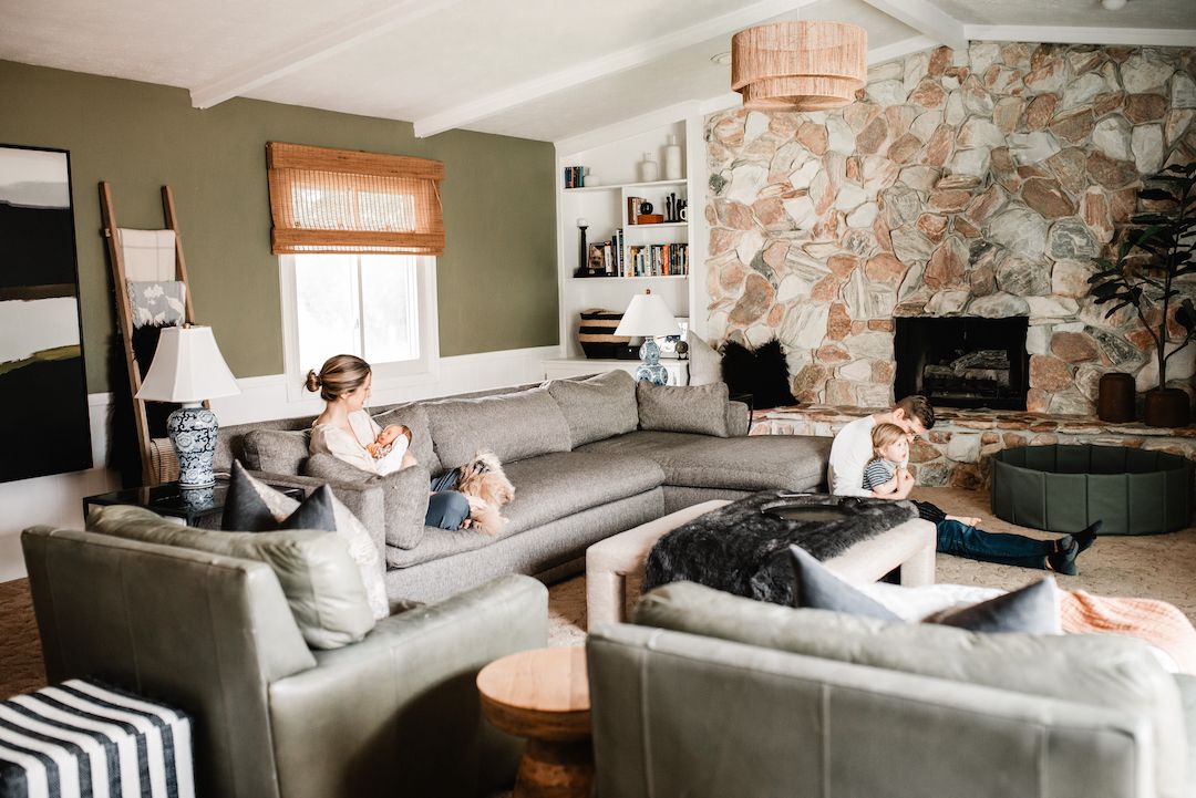 A woman relaxes on a large gray sectional sofa in a modern living room with a stone fireplace.