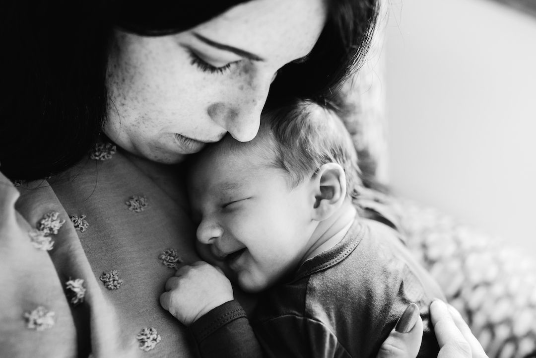 Black and white photo of a mother tenderly holding her smiling newborn baby close to her chest.