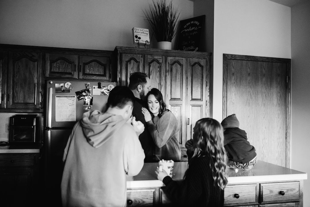 Black and white photo of a family sharing an intimate moment together in a rustic kitchen.