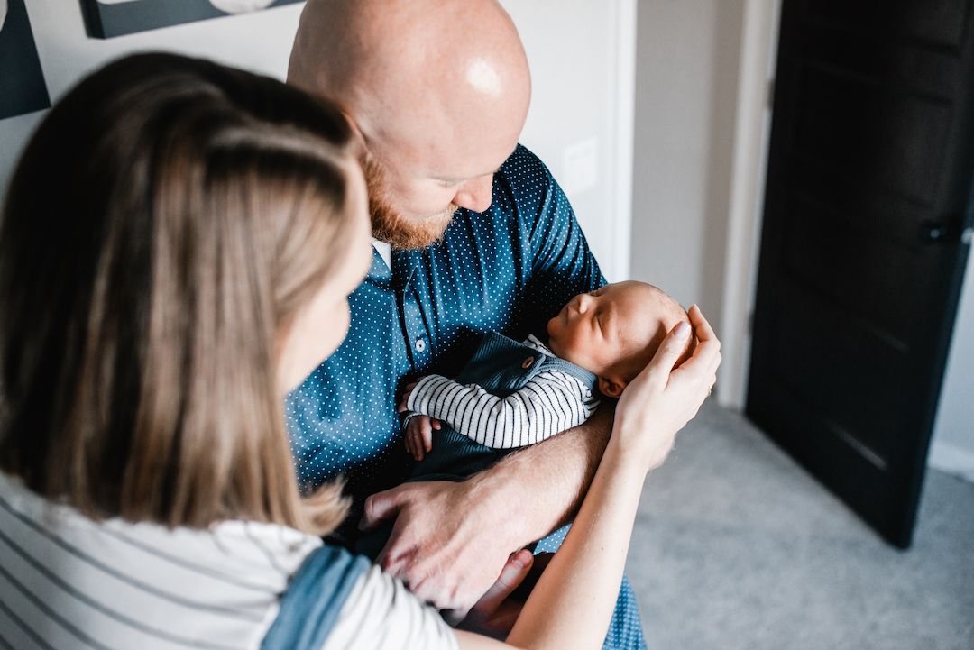 New parents lovingly cradling their newborn baby together indoors in a tender family moment.