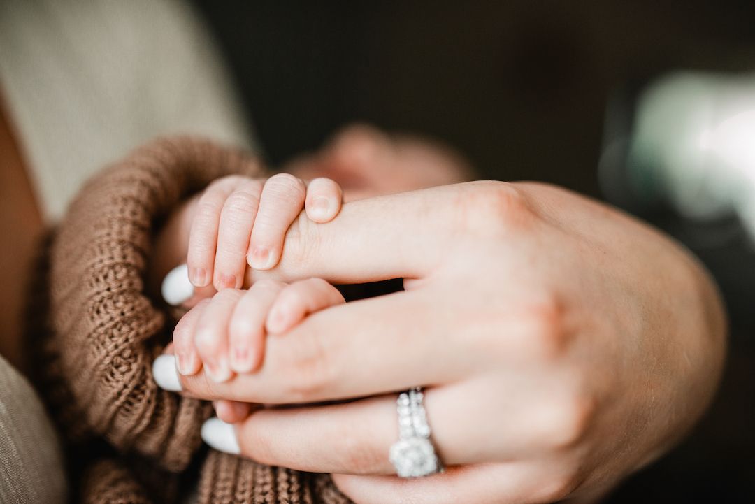 Close-up of couple holding hands, woman wearing diamond engagement ring and brown knit sweater.