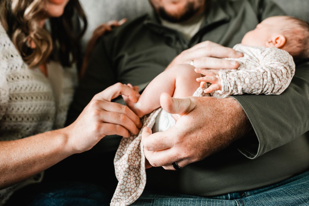 Parents tenderly holding their newborn baby, with mother touching infant's tiny hand in a cozy home setting.