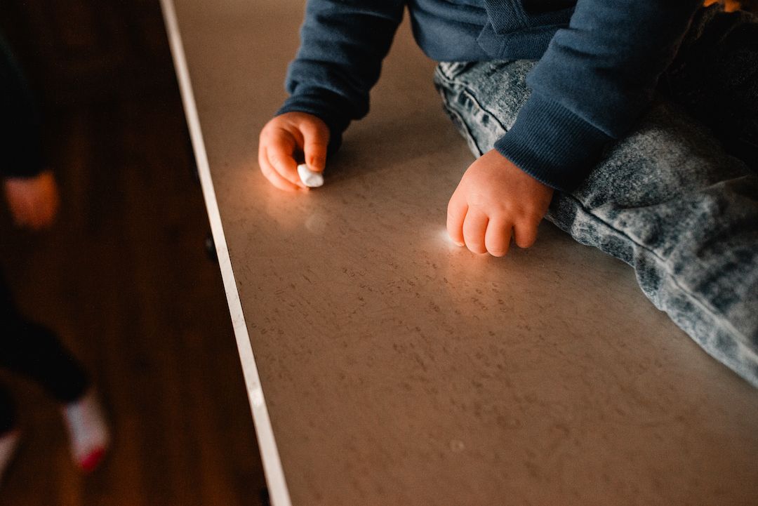 Close-up of a young childs hands holding chalk while leaning against a table edge.