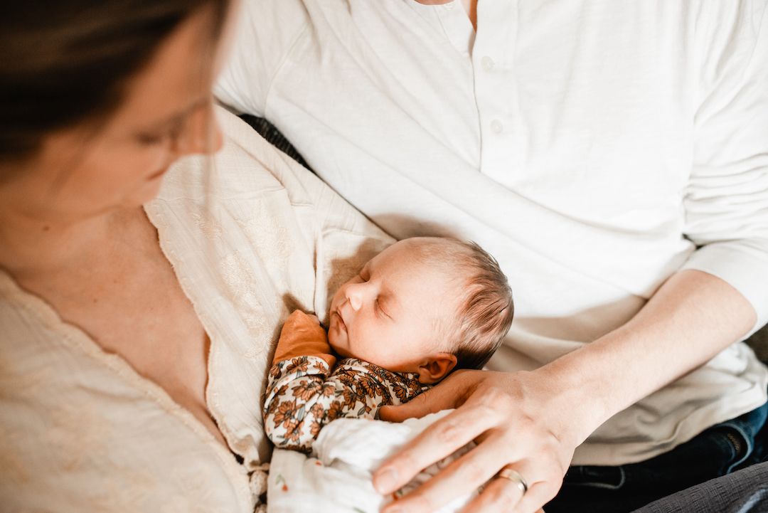 Parents cradling their sleeping newborn baby, captured in a tender and intimate close-up portrait.