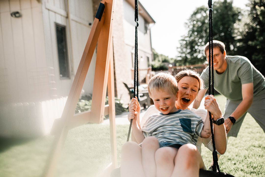 Family enjoying outdoor playtime with a child on a backyard swing set on a sunny day.