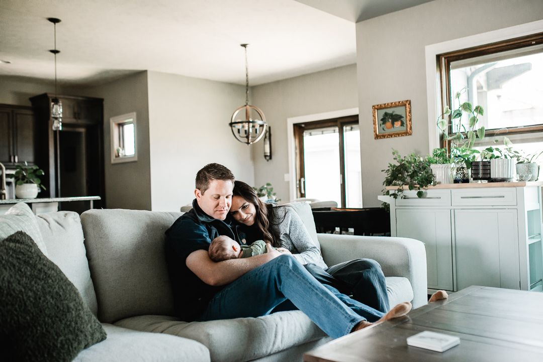 A couple cuddles on a couch holding their newborn baby in a cozy modern living room.