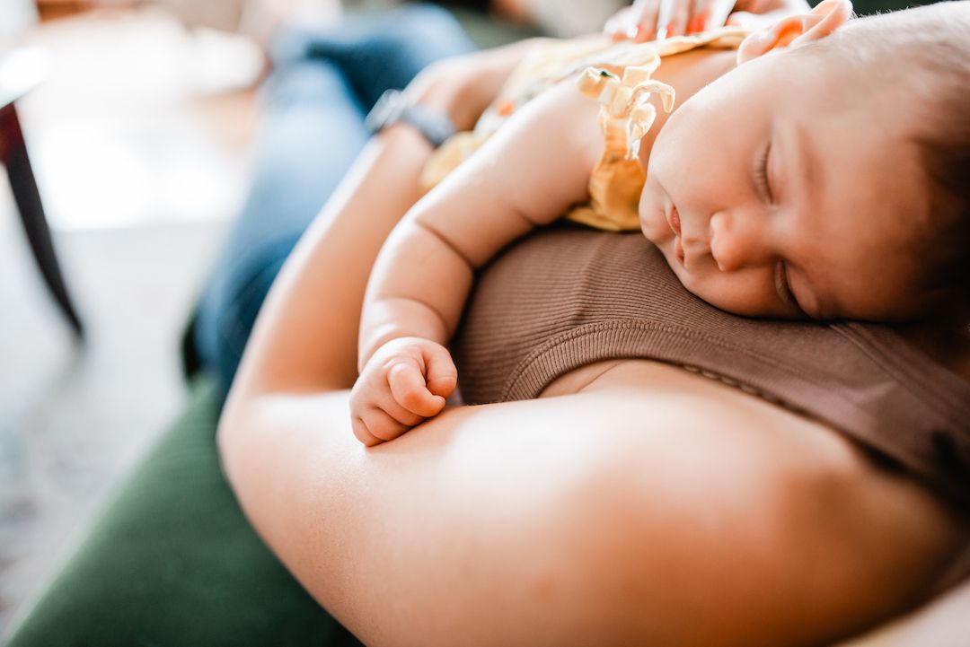 Newborn baby sleeping peacefully on parent's chest, close-up of infant resting on caregiver's arm.