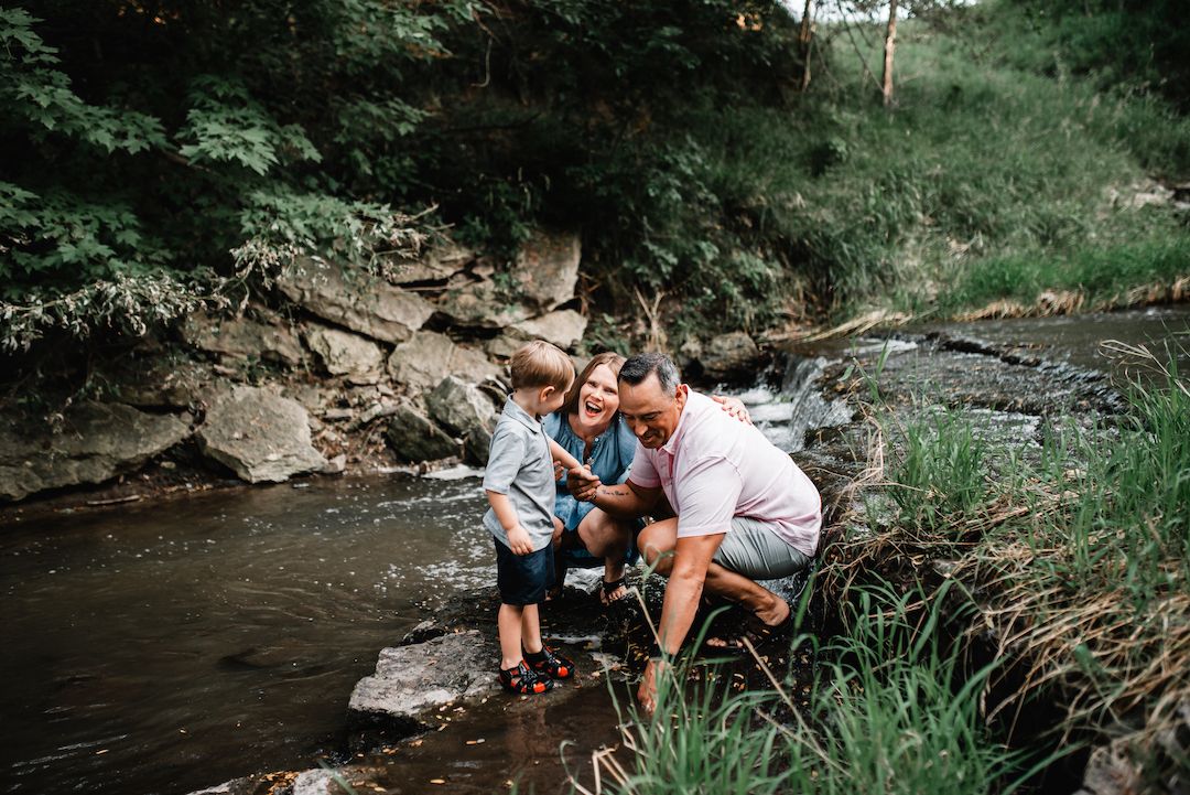 A family of three explores a rocky creek surrounded by lush greenery on a nature outing.