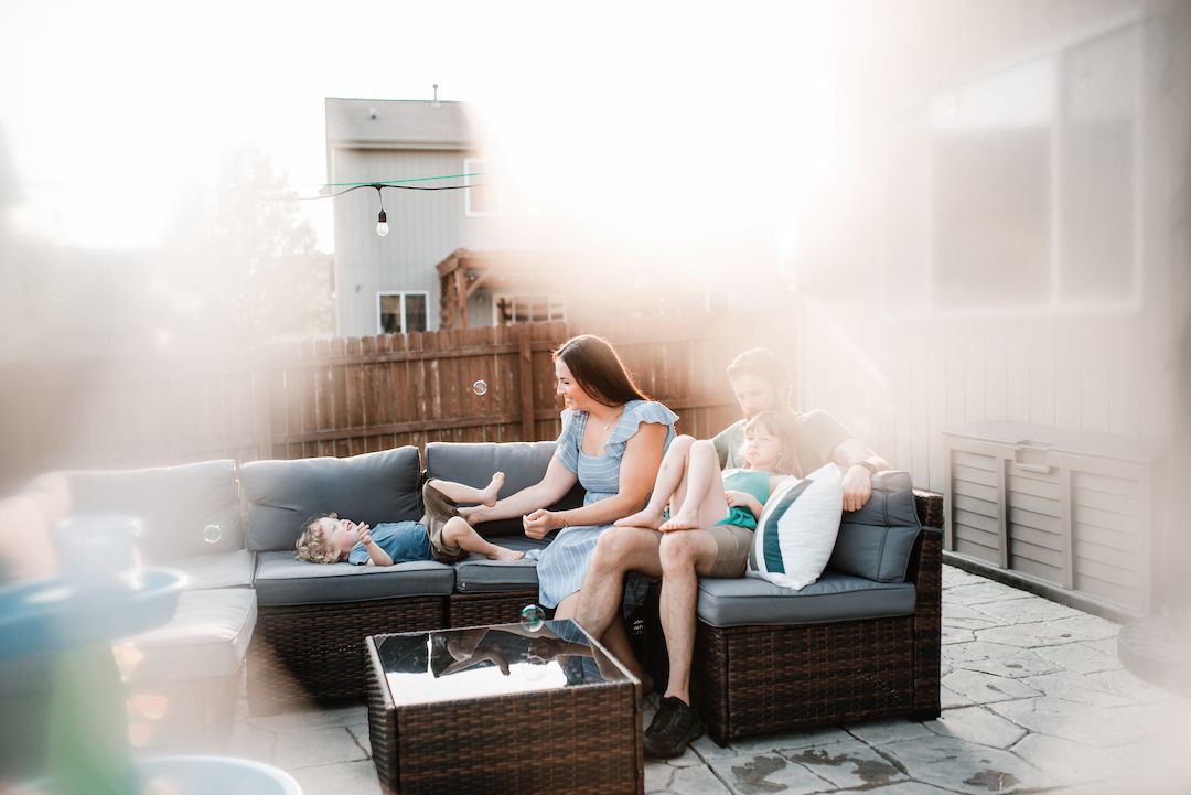 Two women relaxing on outdoor patio furniture with a child on a sunny day.