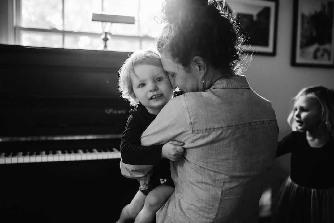 Father holding toddler near a piano in a warm black and white lifestyle family portrait.