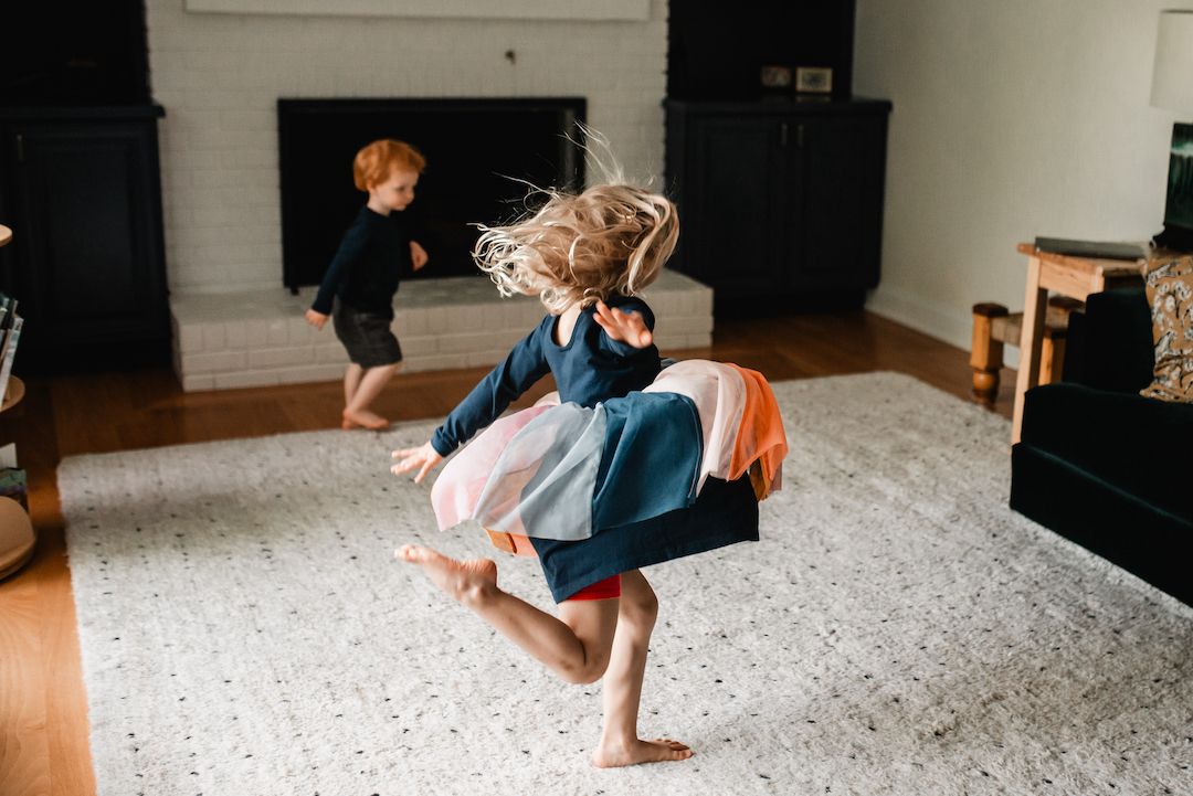 Two energetic children dancing and spinning in a bright modern living room.