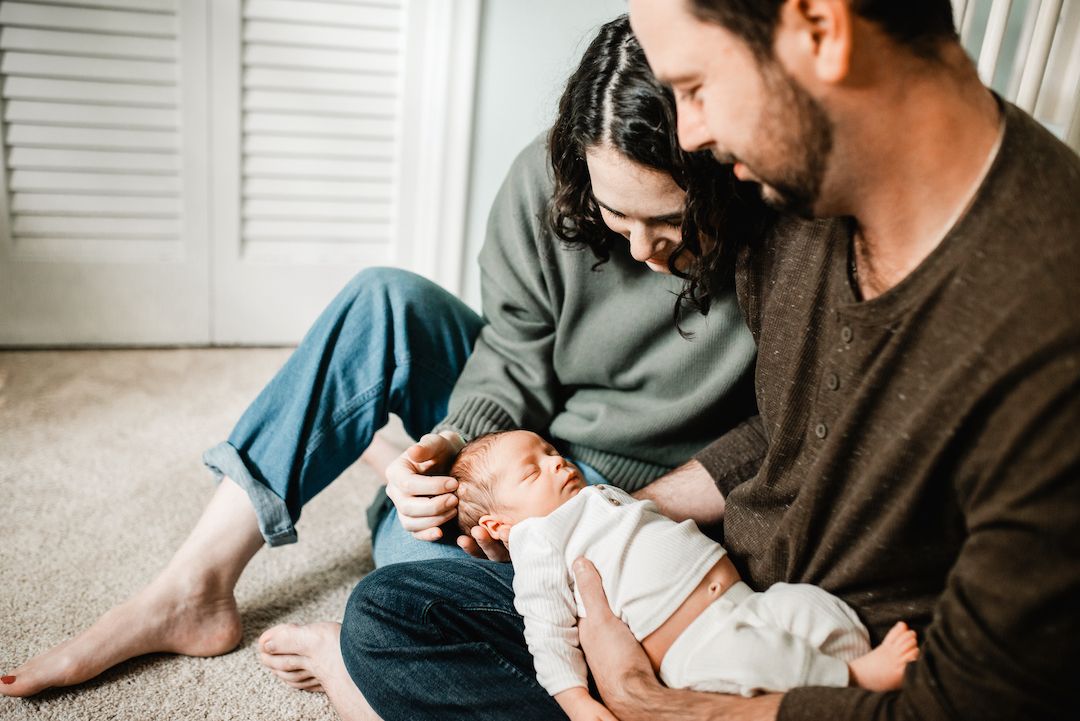 Happy couple sitting on floor admiring their newborn baby in a cozy home setting.