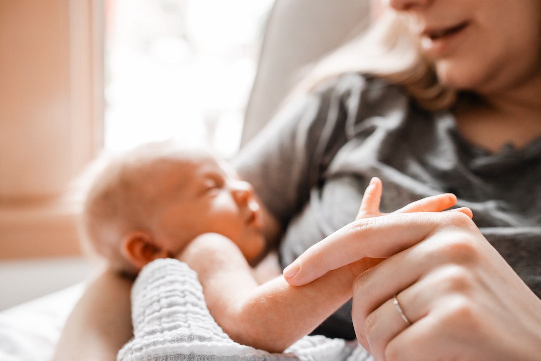 Mother tenderly holding newborn baby's hand while cradling infant in arms indoors.