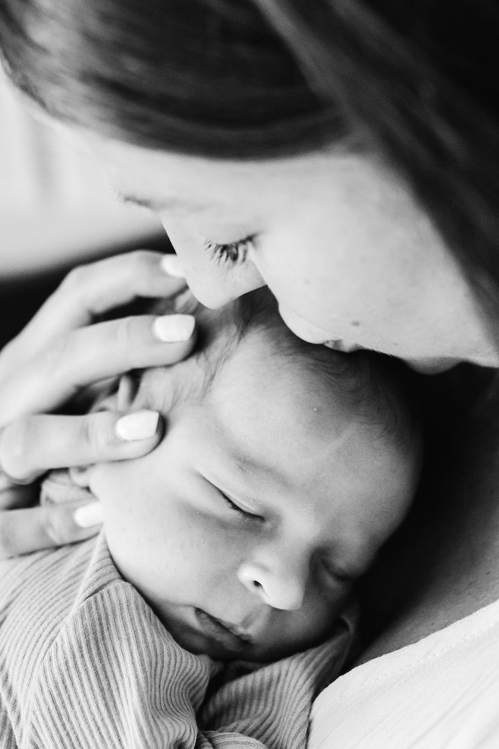 Black and white photo of a mother tenderly kissing her sleeping newborn baby.