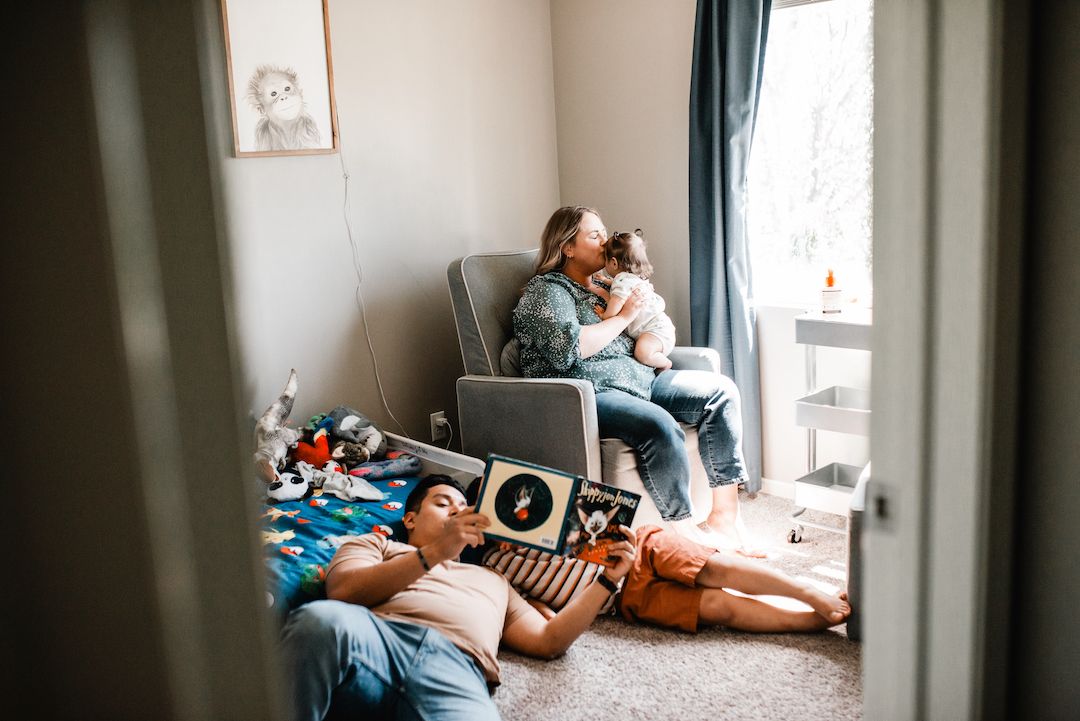Family in a cozy bedroom with father hugging child in chair while boy plays with record player.