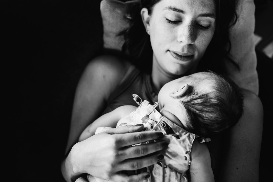 Black and white photo of a mother tenderly holding her newborn baby with medical tubes, sharing a precious moment.