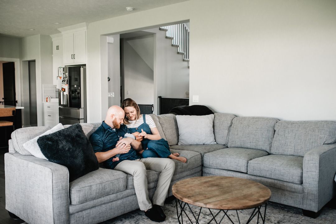 Couple sitting together on gray sectional sofa in modern living room with staircase.