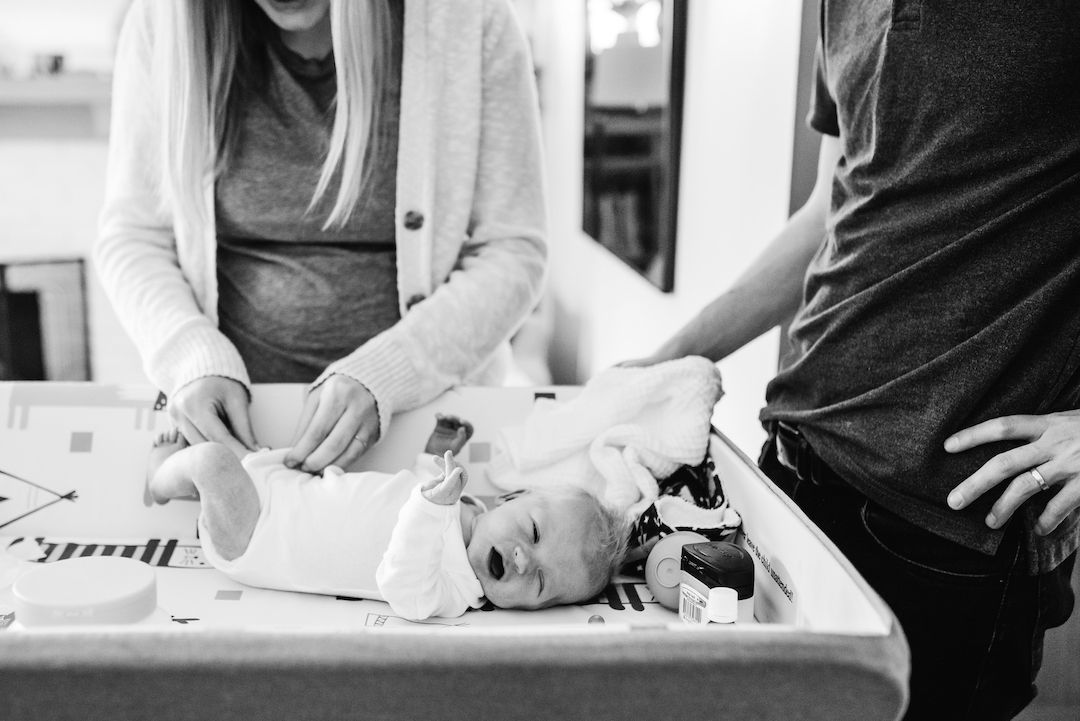 Black and white photo of parents changing newborn baby on changing table at home.