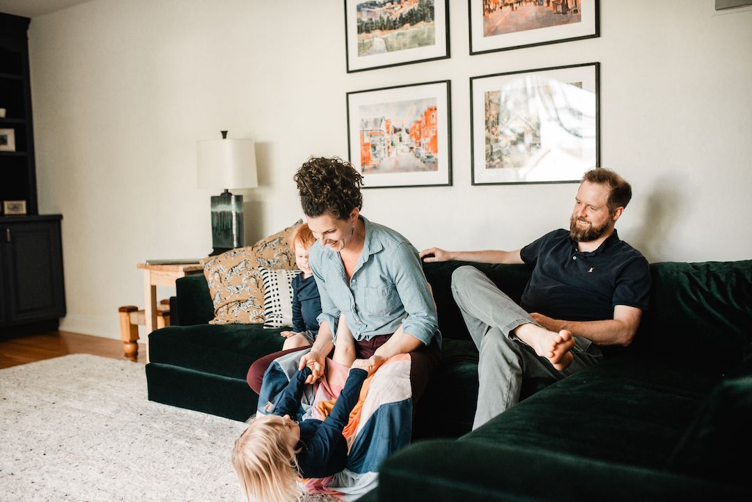 Family relaxing together on green velvet sofas in a cozy living room with framed artwork on the wall.