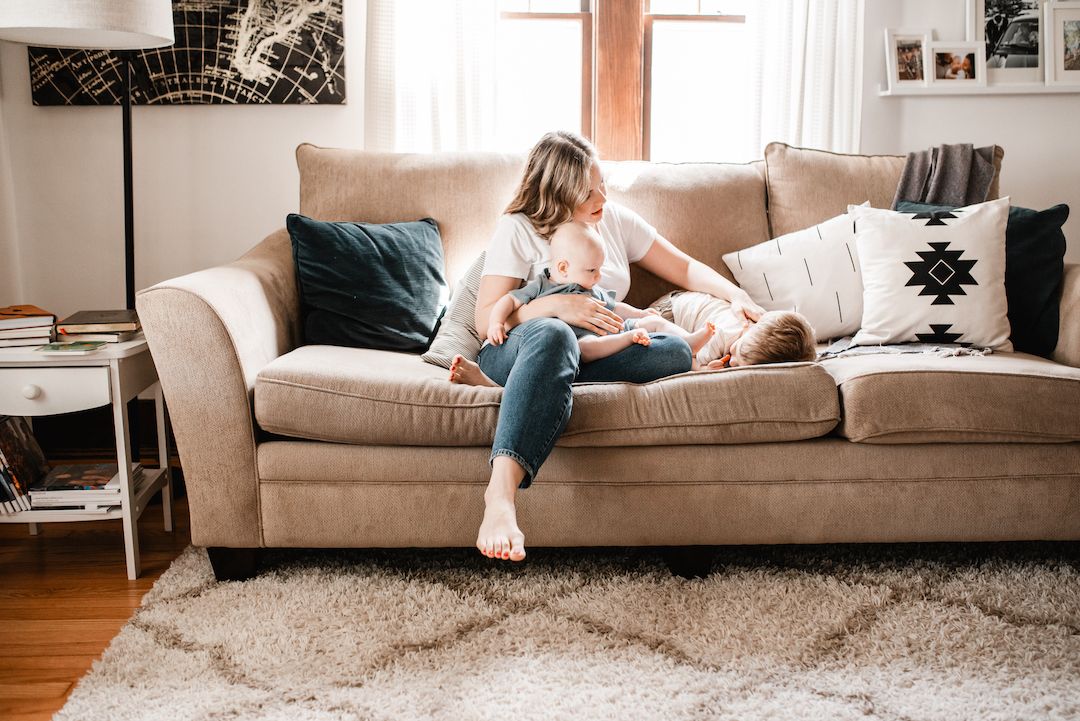 Mother sitting on beige couch interacting with young child in bright cozy living room.