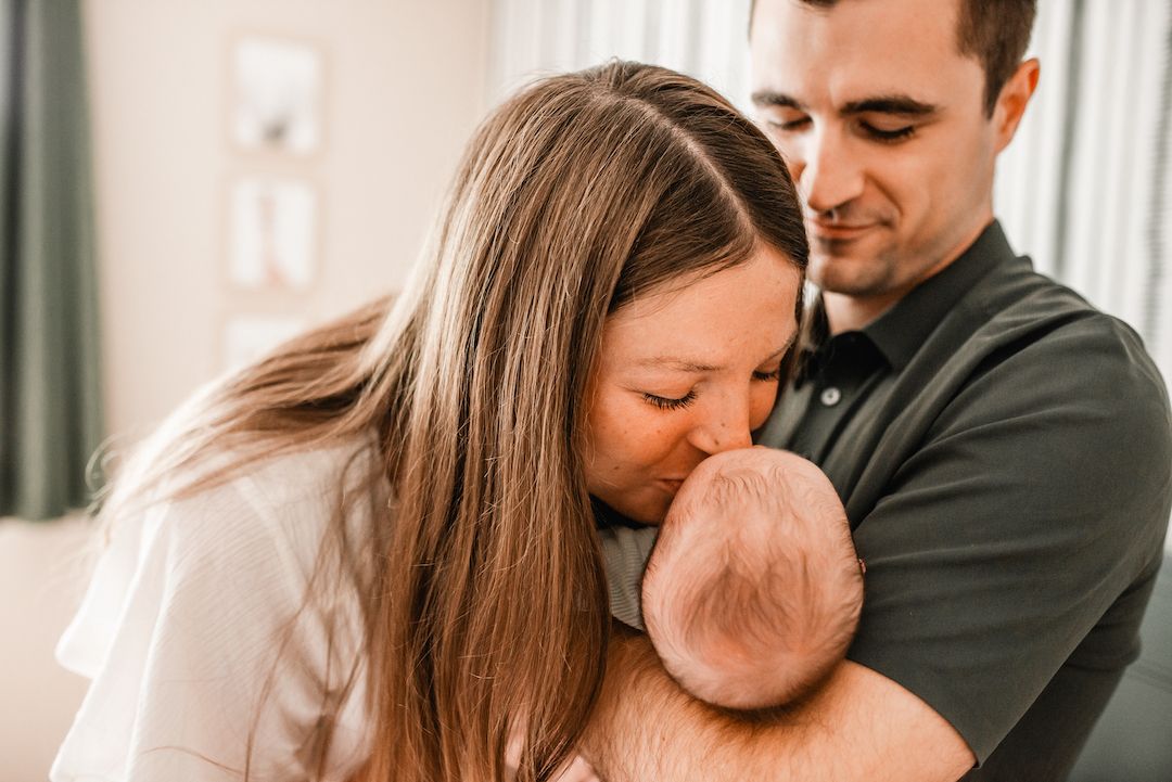 A couple tenderly kisses their newborn baby, sharing a precious family moment together.