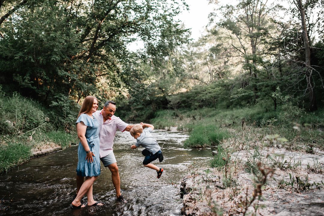 Family playing in a shallow creek surrounded by lush green trees.