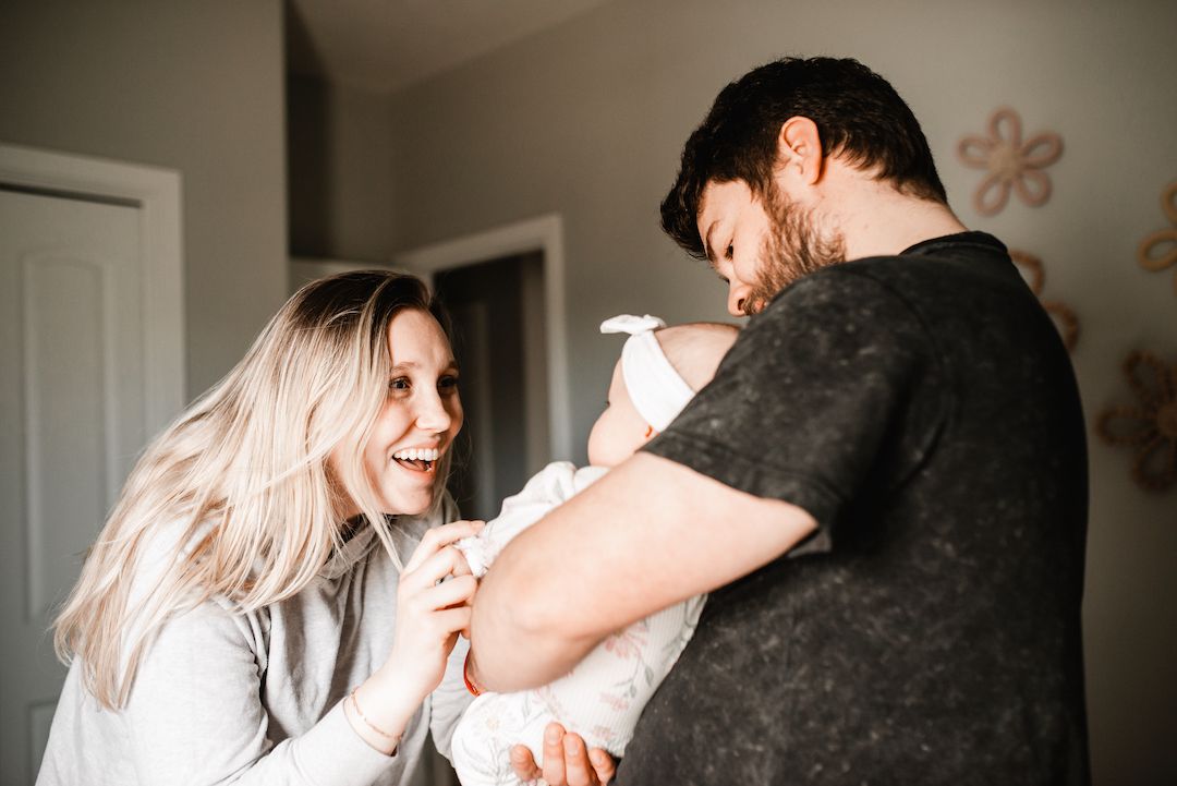 Smiling new parents lovingly hold their newborn baby together in a cozy home setting.