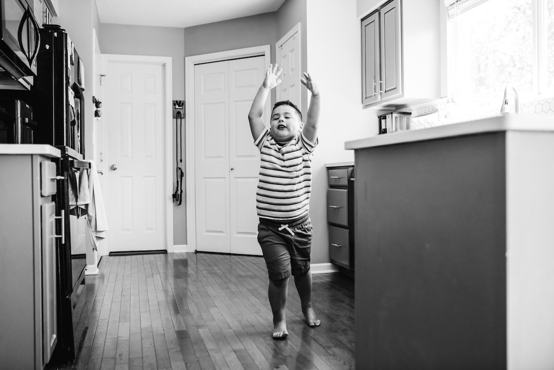Joyful young boy jumping with arms raised in a modern kitchen in black and white.