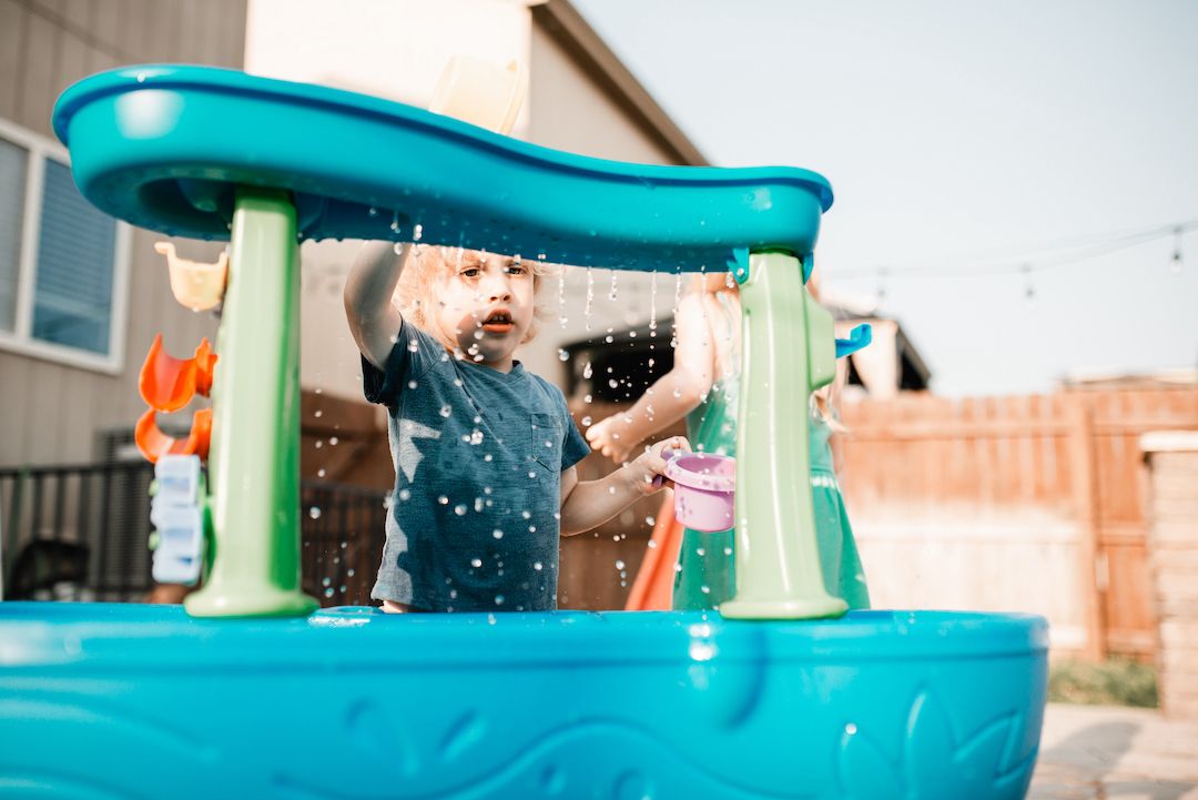 Toddler playing with water table toy in sunny backyard on summer day.